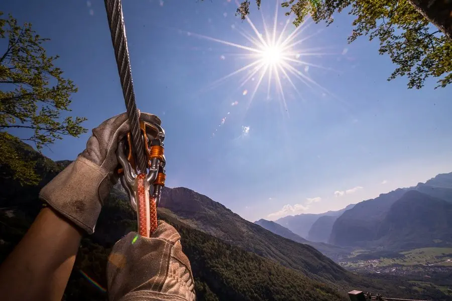 Close-up picture of a hand in gloves holding a carabiner with a scenic background