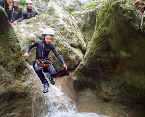 Boy jumps to the river from rocks in a full safety gear