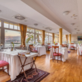 Hotelska restavracija s polno obloženimi mizami in pogledom na jezero