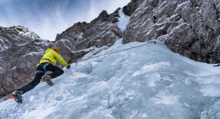Person in a full safety gear is climbing an icy rock formation
