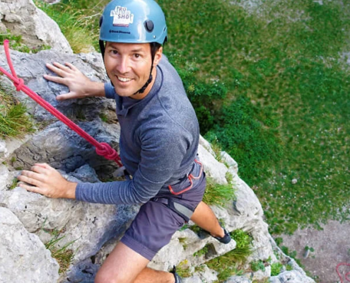 Smiling rock climber is seen from above as he ascends on rocky path in a full safety gear