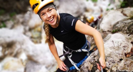 Girl is seen smiling and climbing on a rock formation in a full safety gear