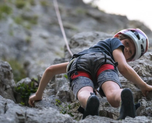 Boy is seen from the ground level while climbing a rock formation in full safety gear