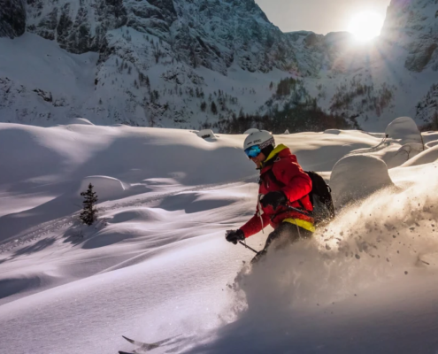 Person skiing through deep powder snow on a sunny day in a mountainous winter landscape, surrounded by snowy peaks and pine trees.