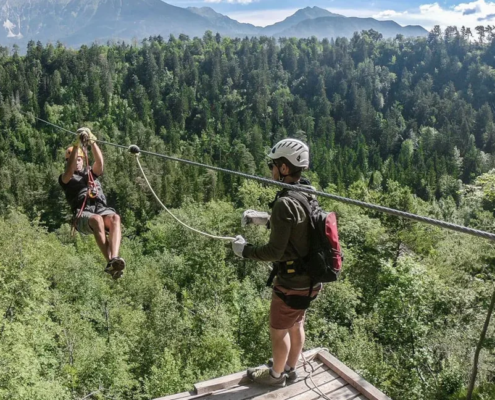 Man zip-lining on a sunny day with scenic forest and mountain background