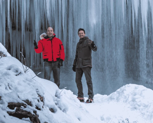 Slovenia winter activities: Two man showing thumbs up while standing under frozen waterfall