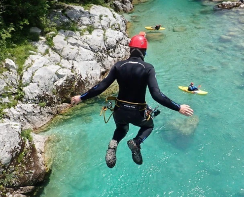 Canyoning Slovenia: A person jumping from a bridge into the emerald-colored Soca River.