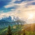 Hiking Slovenia: Scenic view of a mountain range with a golden sunset and lush greenery in the foreground.