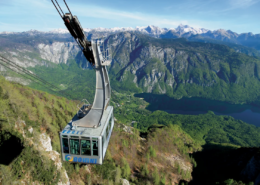 Bled Tours: Cable car ascending over green mountain slopes with dramatic peaks and a winding river visible in the expansive valley below.