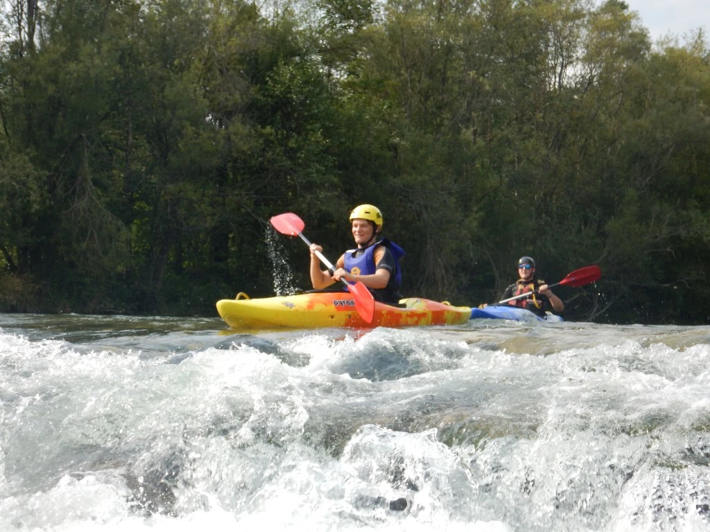 Kayaking Kayaking Slovenia: Kayaker maneuvering through small whitewater rapids in a bright yellow kayak on a sunny day.