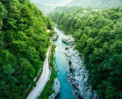 Bled Tours: An aerial view of the turquoise Soca River winding through dense green forest within the beautiful Triglav National Park in Slovenia.