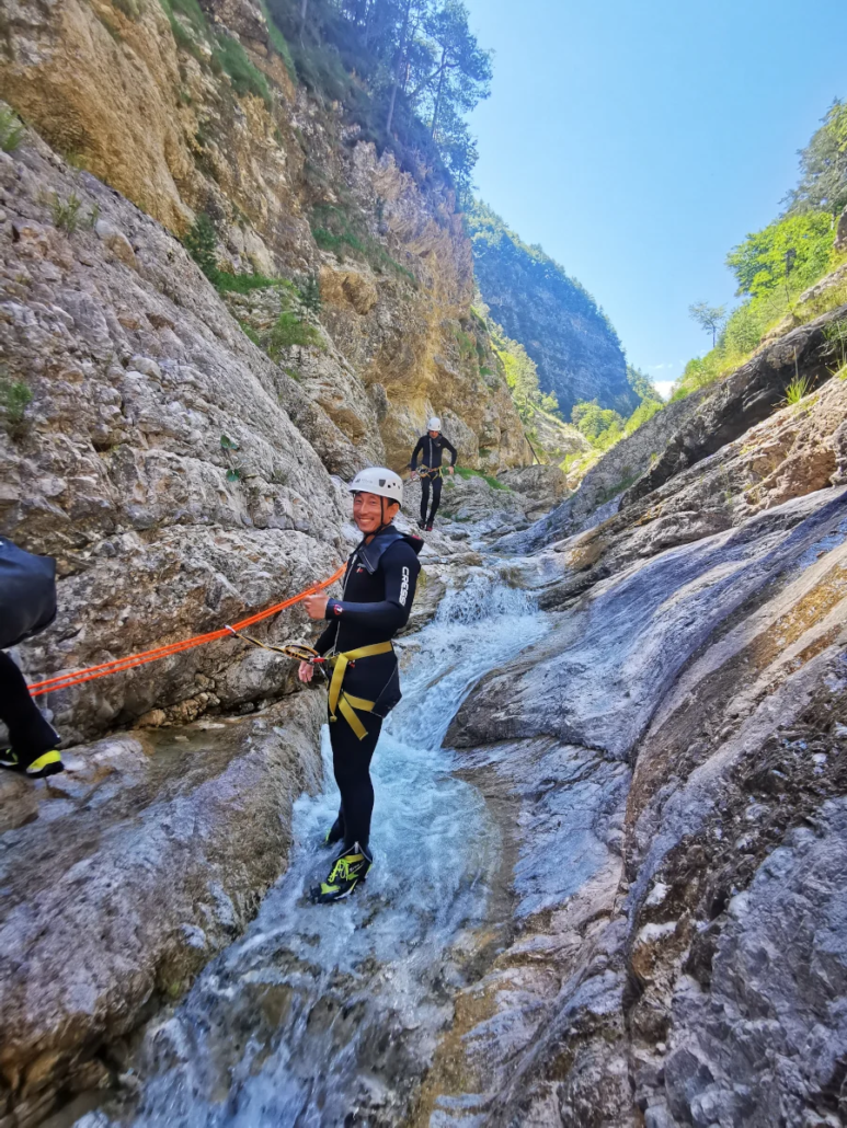 Group walking through a carved-out water channel in bright canyon light, ready for descent.