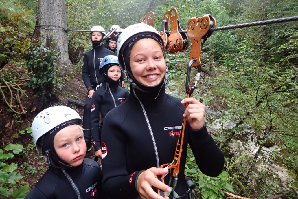 Smiling group of canyoners in wetsuits preparing gear in a lush forest setting before the descent.