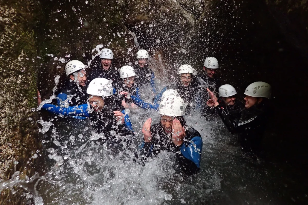 Group of people in helmets getting splashed by canyon water in a narrow, dark rock corridor.
