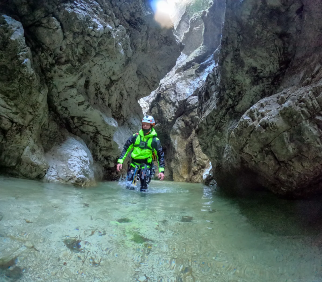 Person wading through shallow, crystal-clear water inside a high-walled rocky canyon.