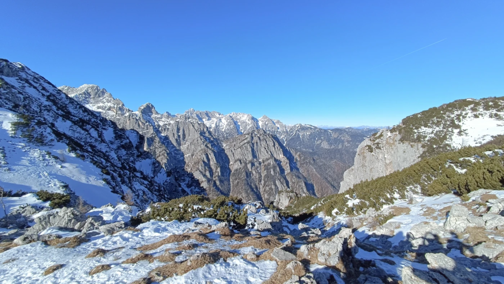 Snow-covered slopes and rocky ridges of Debela Peč under a clear blue sky in winter