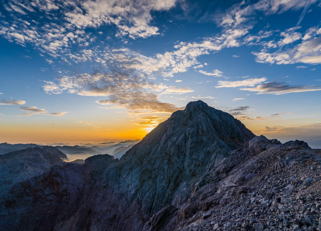 Sunset casting warm colors over Mount Triglav and surrounding peaks under a partly cloudy sky