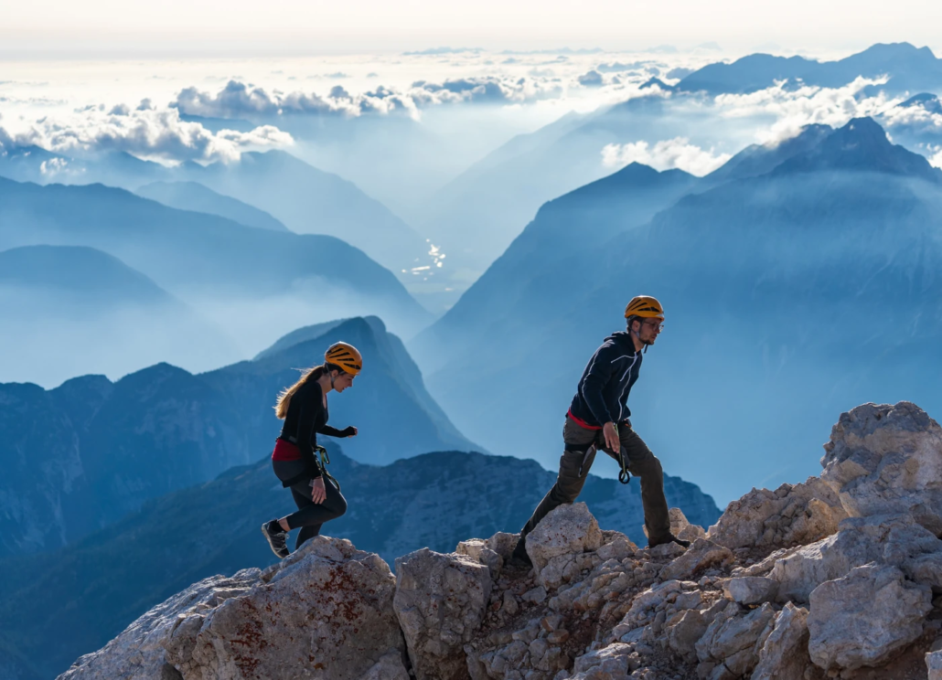 Two climbers ascending an exposed rocky ridge with dramatic mountain views on the final steps toward Mount Triglav summit