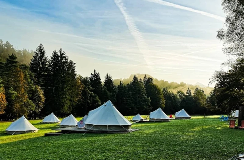 Eco River Camp with white canvas tents on a grassy field surrounded by forest