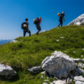 Group of hikers walking uphill on a grassy meadow with rocks, under a clear blue sky in the Triglav mountains
