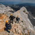 Climbers taking a break on a rocky mountain ridge with dramatic peaks in the background on Triglav
