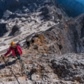 Mountaineers using safety gear while climbing a narrow rocky ridge on Triglav with steep cliffs around