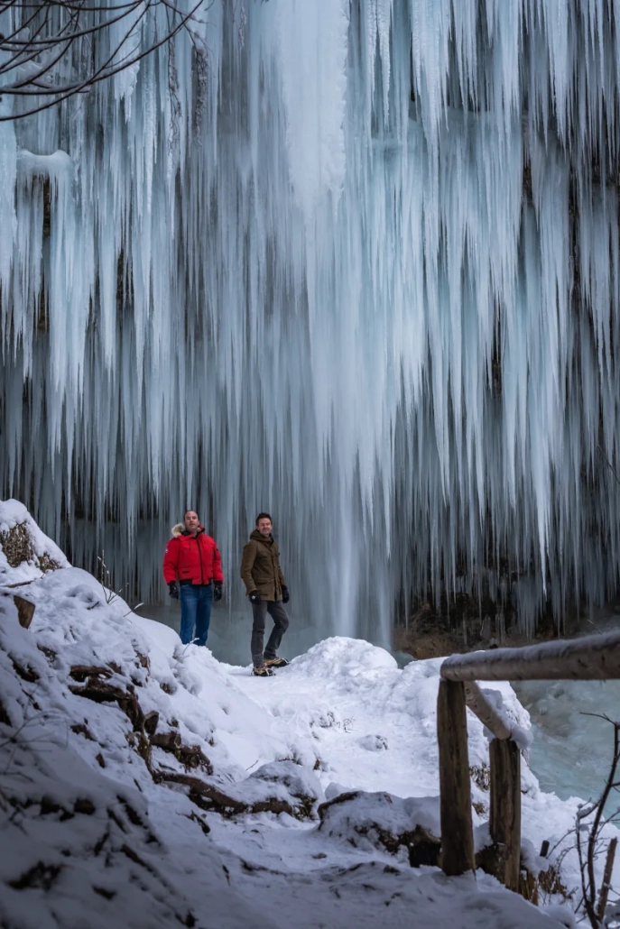 Two people near frozen Peričnik Waterfall with icicles