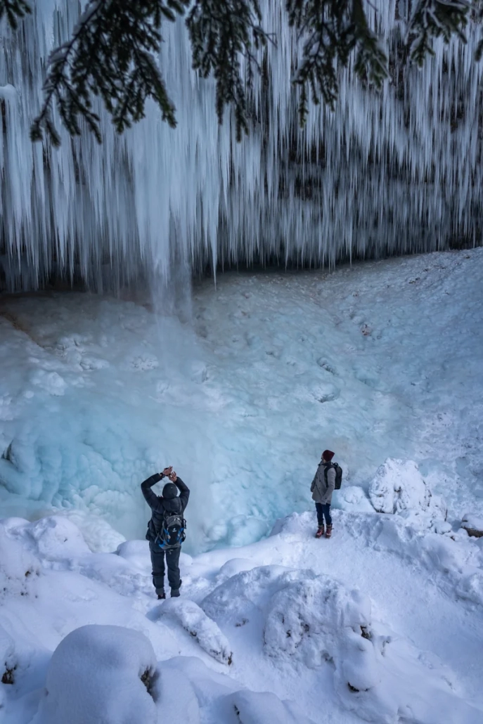 Hikers on snowy path below frozen Peričnik Waterfall