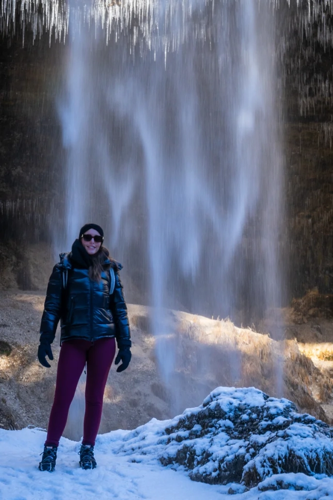 Person standing beneath frozen Peričnik Waterfall in winter